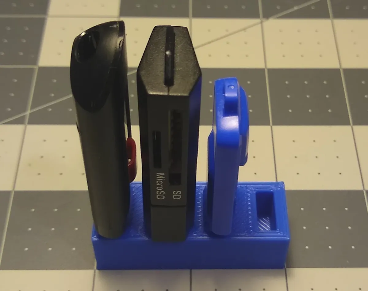 A blue printed organizer holding USB drives and a card reader on a cutting mat.