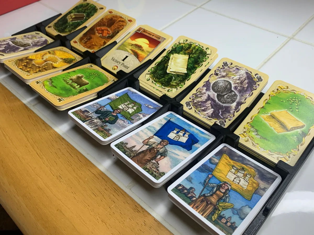 Catan resource and development cards arranged in connected black and white printed card trays.
