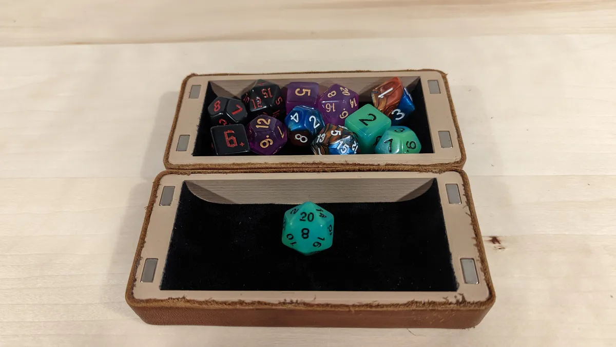 An open brown dice box with a set of colorful dice in one half and a green die in the lined rolling tray.