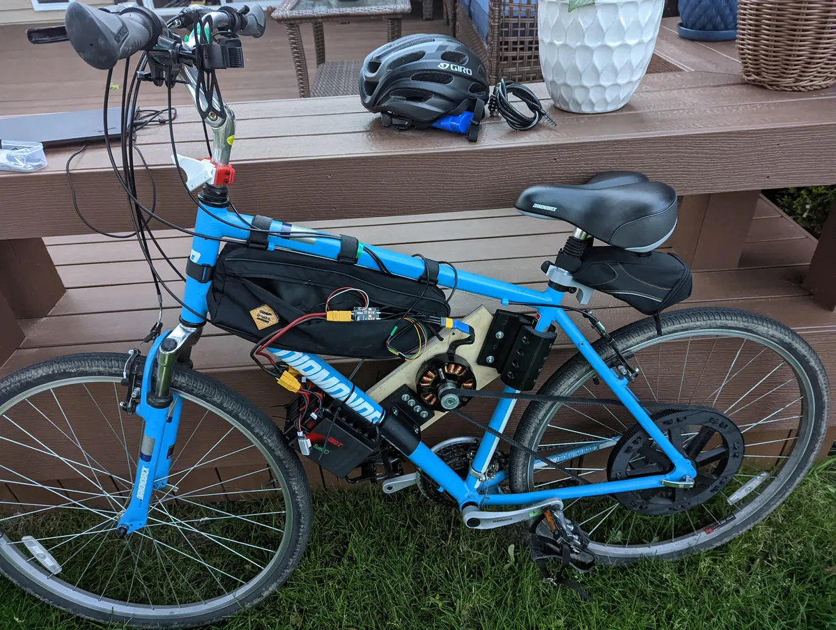 A blue bicycle fitted with a custom motor mount, large rear pulley, belt drive, and electronics.