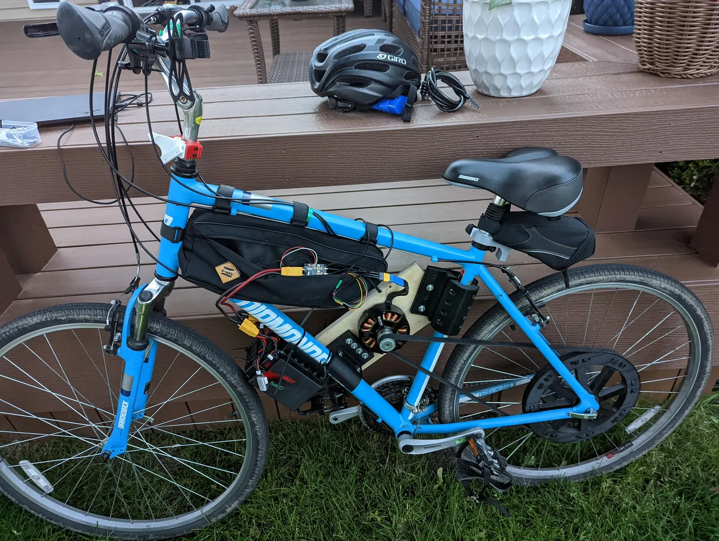 A blue bicycle fitted with a custom motor mount, large rear pulley, belt drive, and electronics.