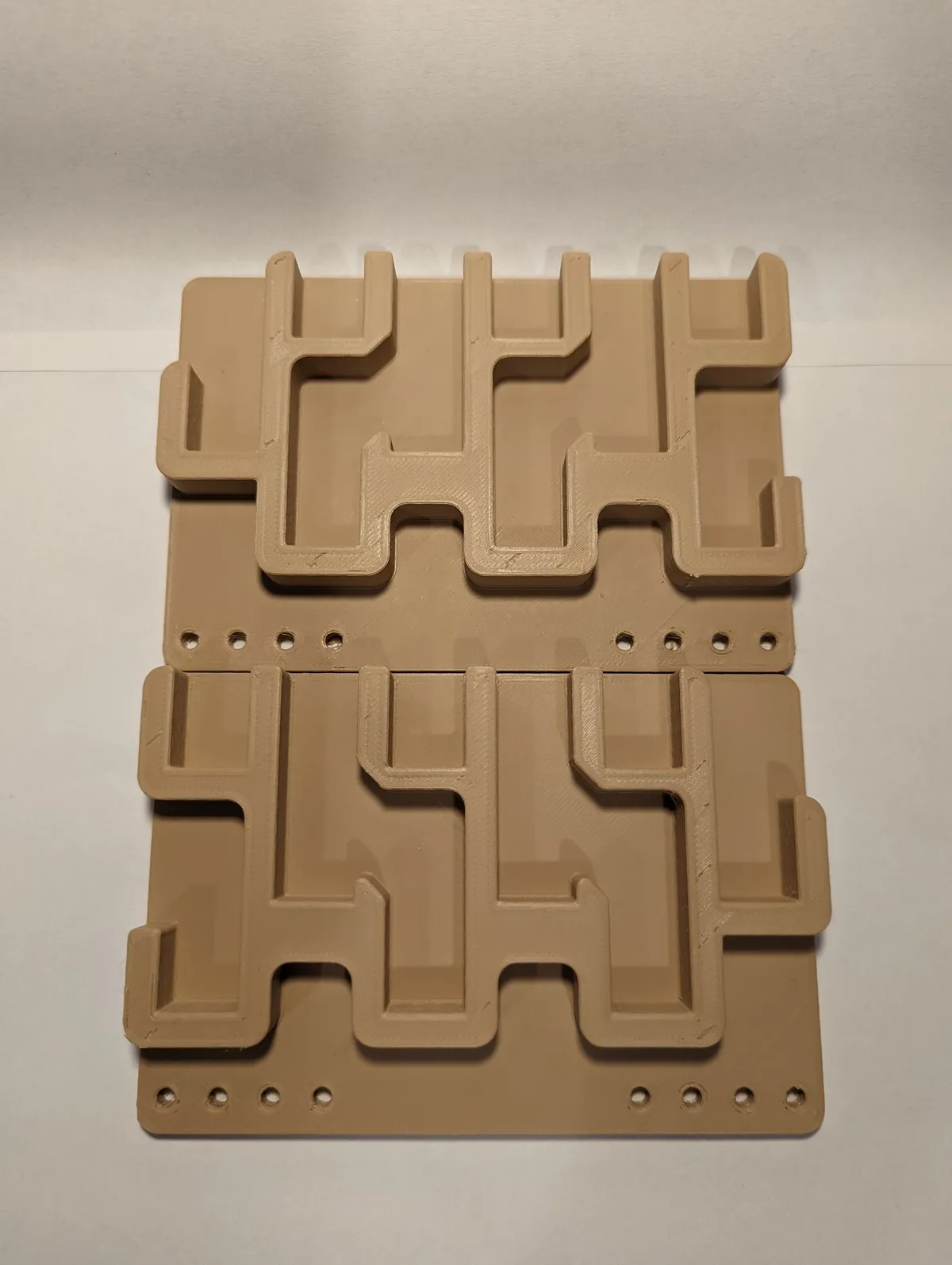 Two tan three-row holder panels laid one above the other, showing stepped hook-shaped slots and a line of mounting holes on each panel.