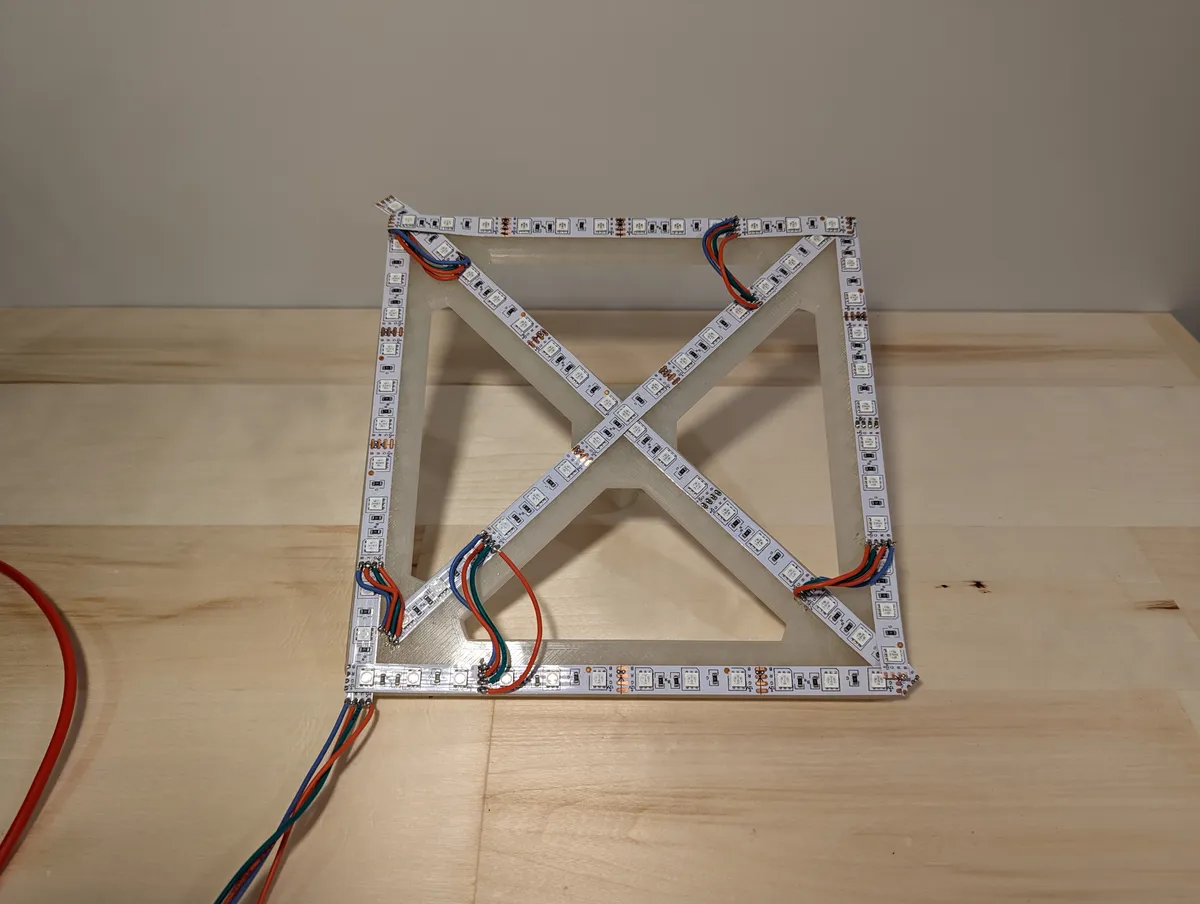 An open geometric frame on a desk with exposed LED strips following its edges and diagonals.