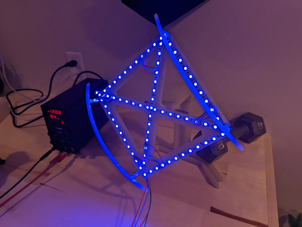 An open-frame geometric sculpture glowing blue at its edges on a workbench.