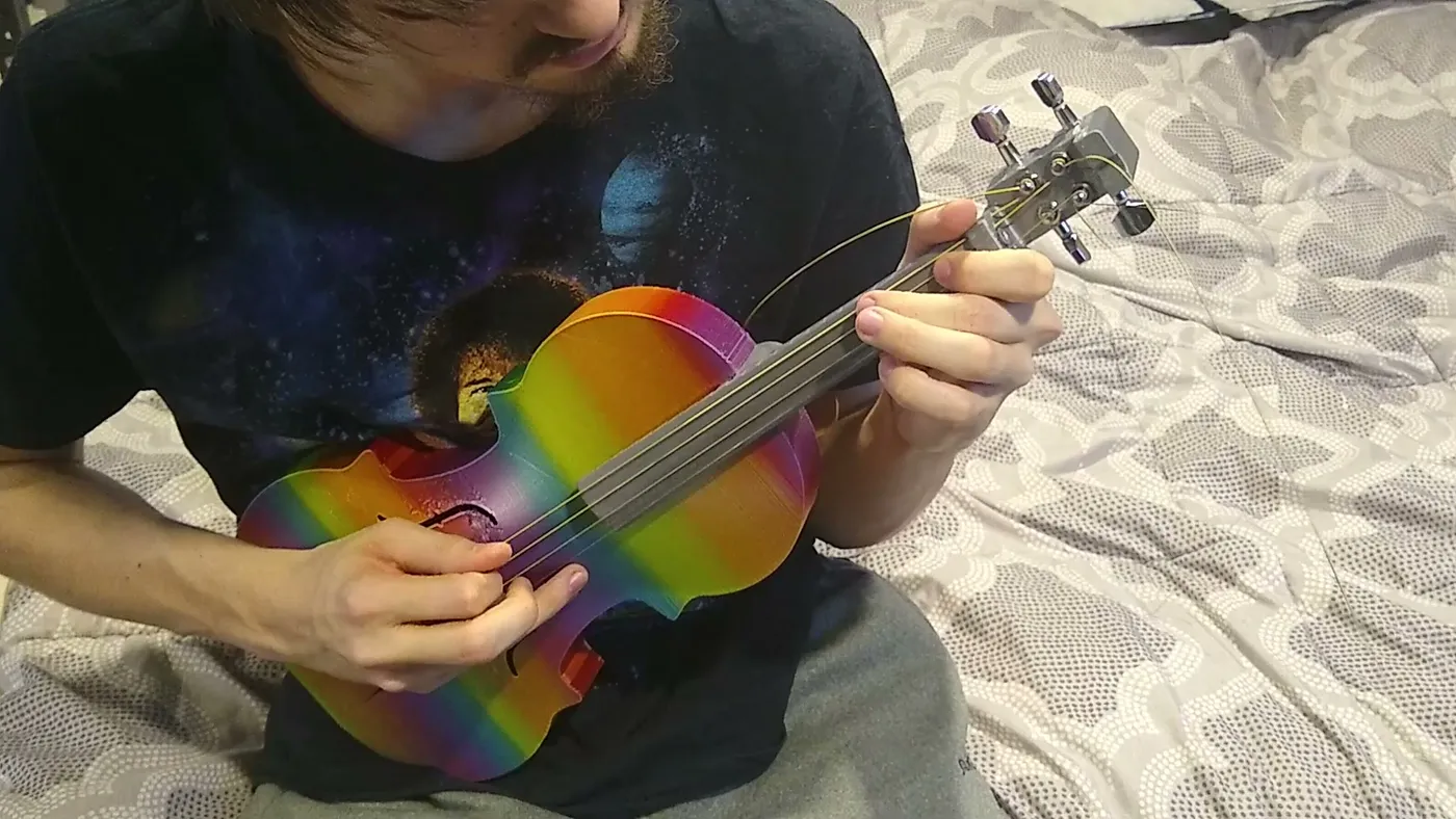 Playing a rainbow-colored printed violin fitted with a gray neck, four strings, and guitar tuning machines.