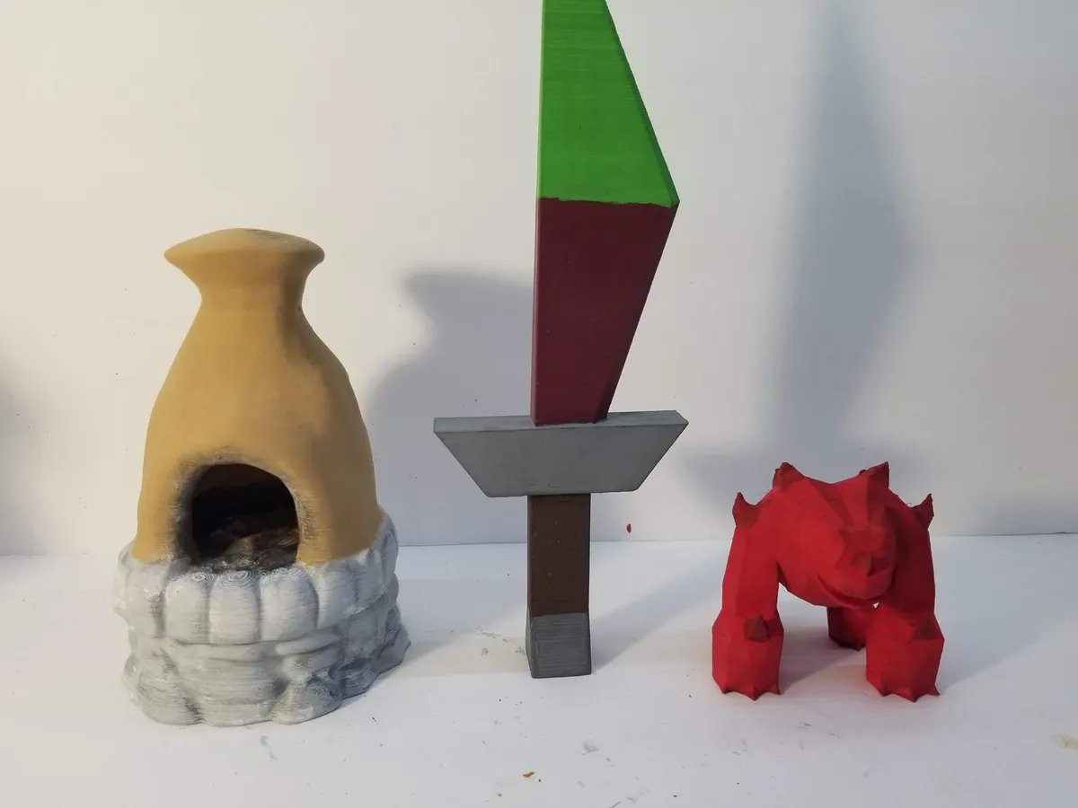 A painted dagger and red Jad figure beside a miniature furnace on a white photo backdrop.