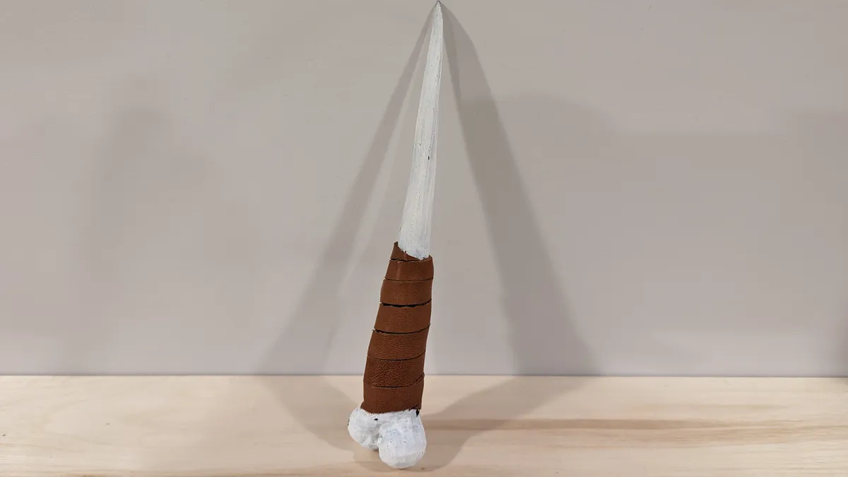 A printed bone-knife display prop with a white blade and brown wrapped handle.