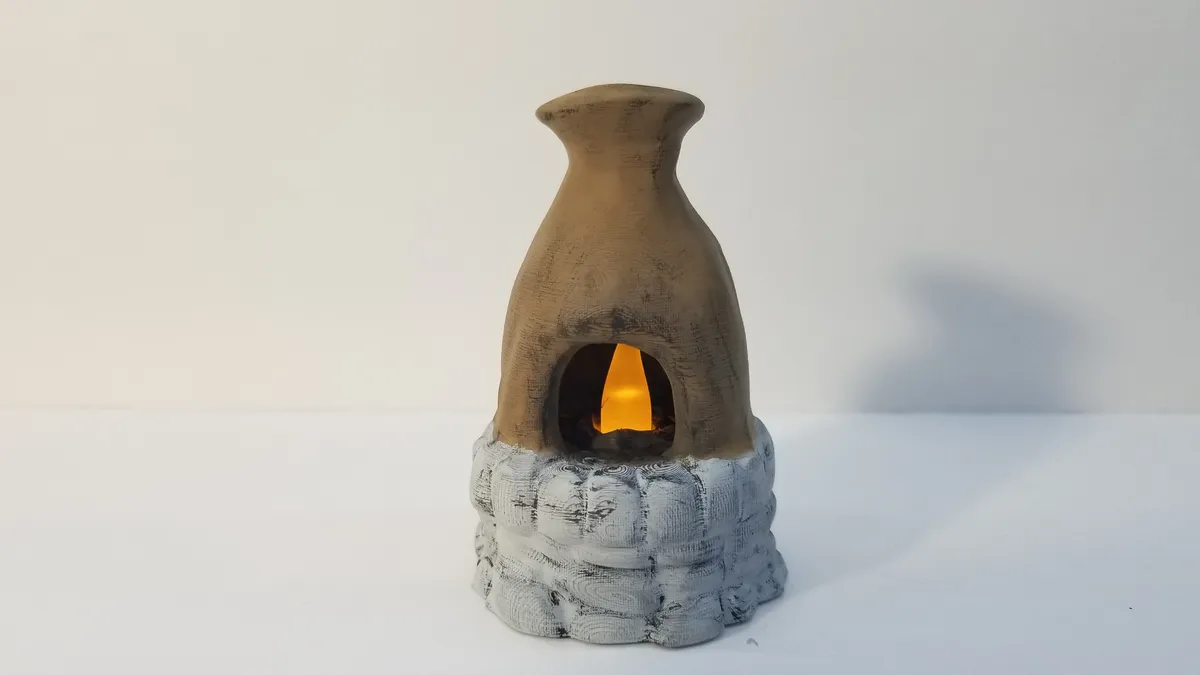 A finished miniature furnace with a weathered tan chimney, gray base, and warm light inside.